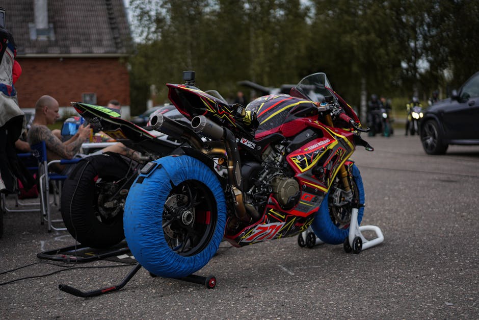 A vibrant racing motorcycle with tire heaters in a pit area, ready for the race.