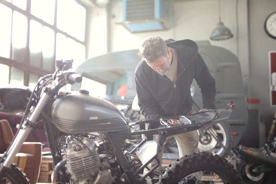 Man working on a motorcycle inside a workshop, focusing on repair and maintenance tasks.