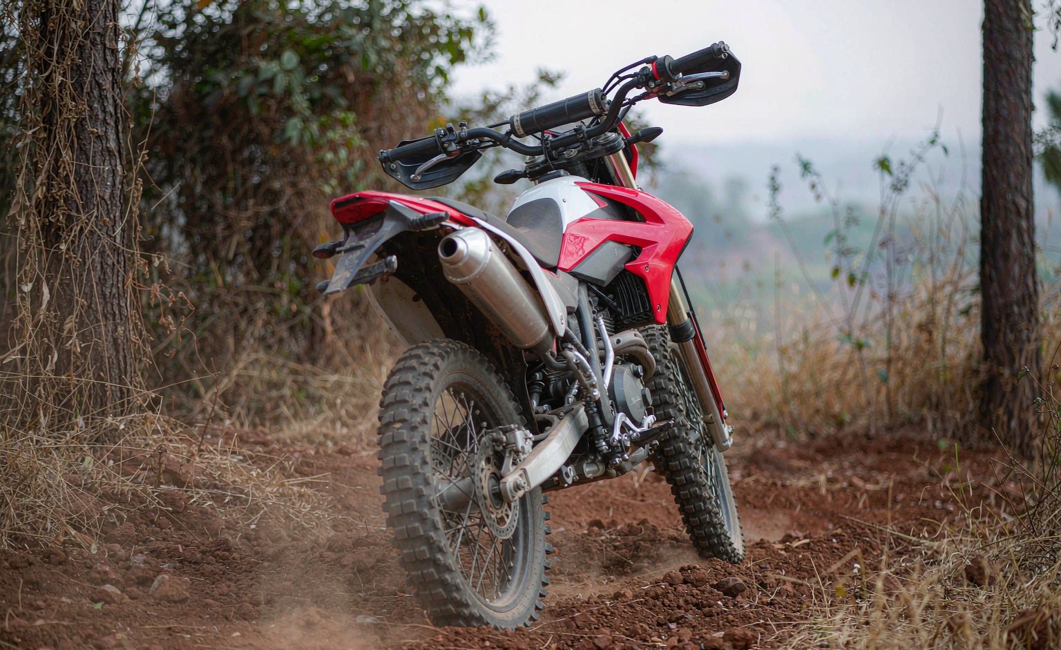 Dirt bike motorcycle on a red dirt trail kicking up light dust with knobby tires