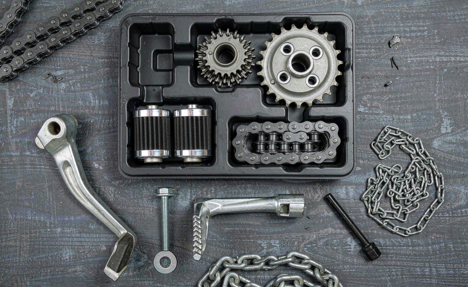 Motorcycle spare parts kit laid out with chain, sprockets, levers and filters in a foam tray